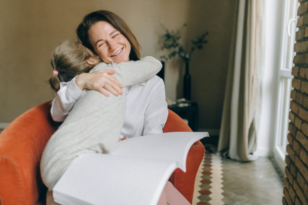 A warm moment between a mother and daughter embracing while reading braille indoors.